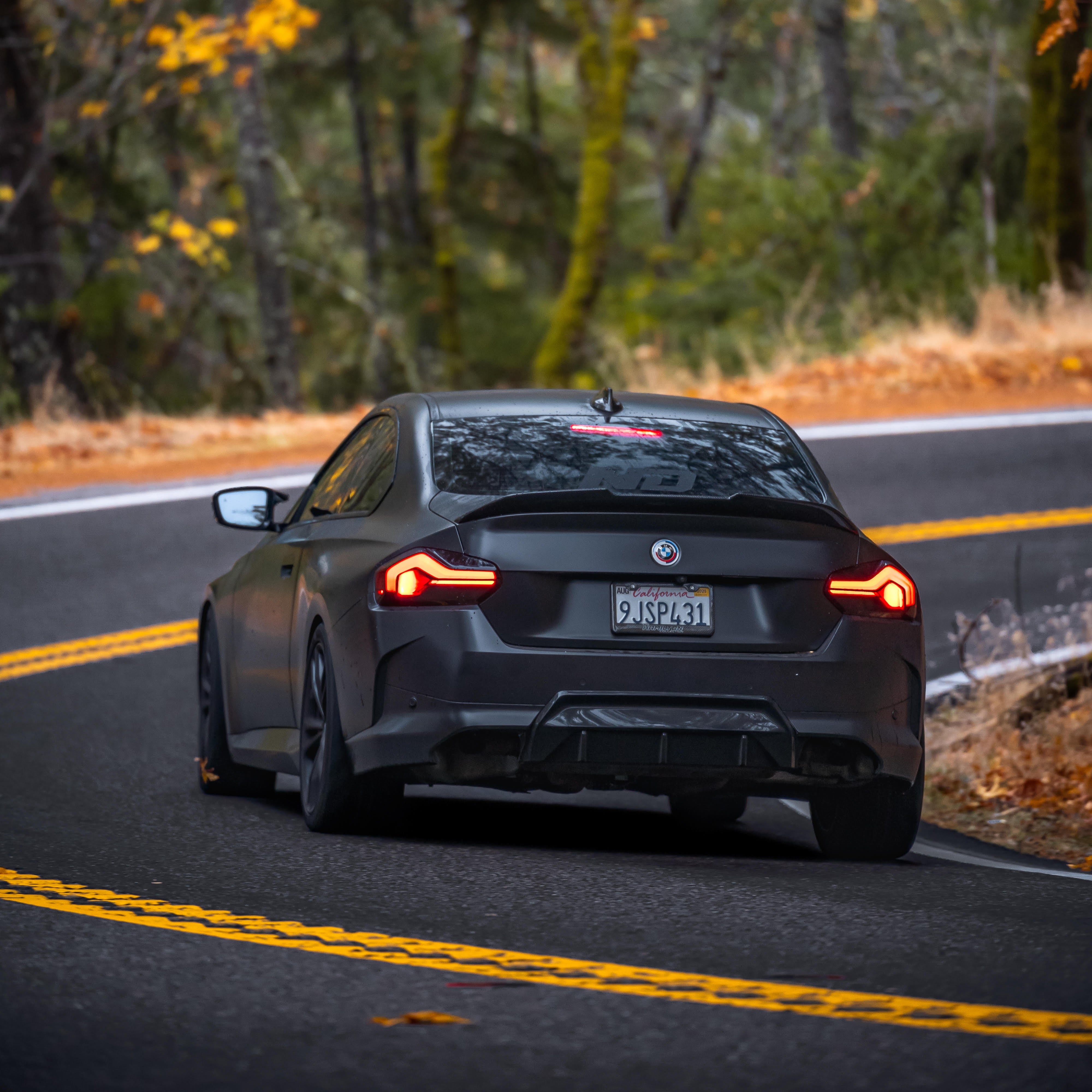 Black car driving on a road with autumn foliage